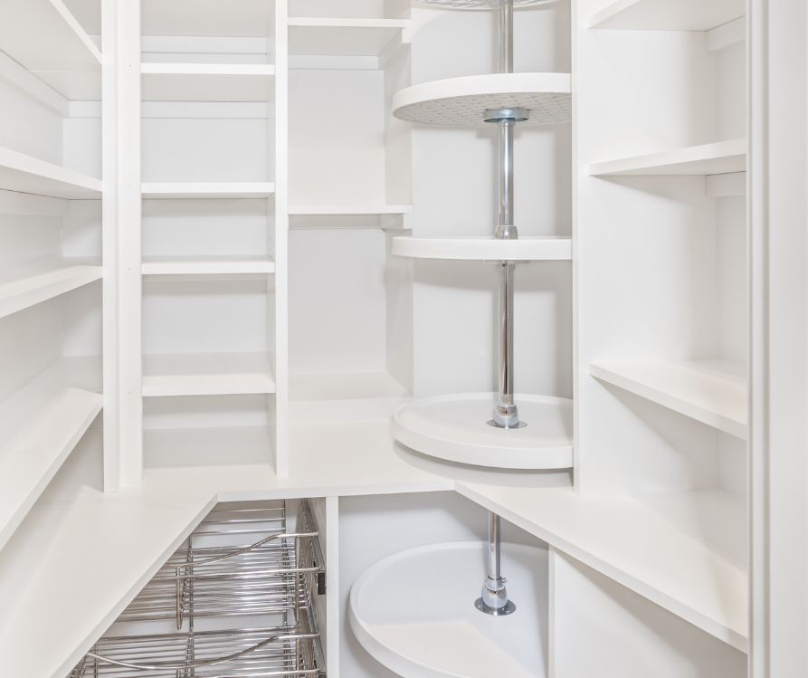 A pantry making the most of an awkward corner with space saving wire baskets, a lazy Susan, and a variety of shelf sizes.