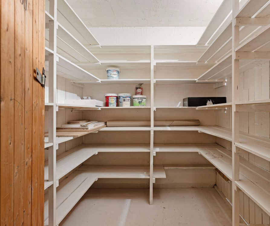 A walk in pantry with a lot of white shelves on each wall.