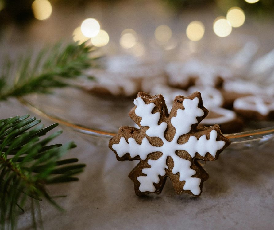 Snowflake shaped ginger cookie topped with white frosting on a wooden table next to pine sprigs.