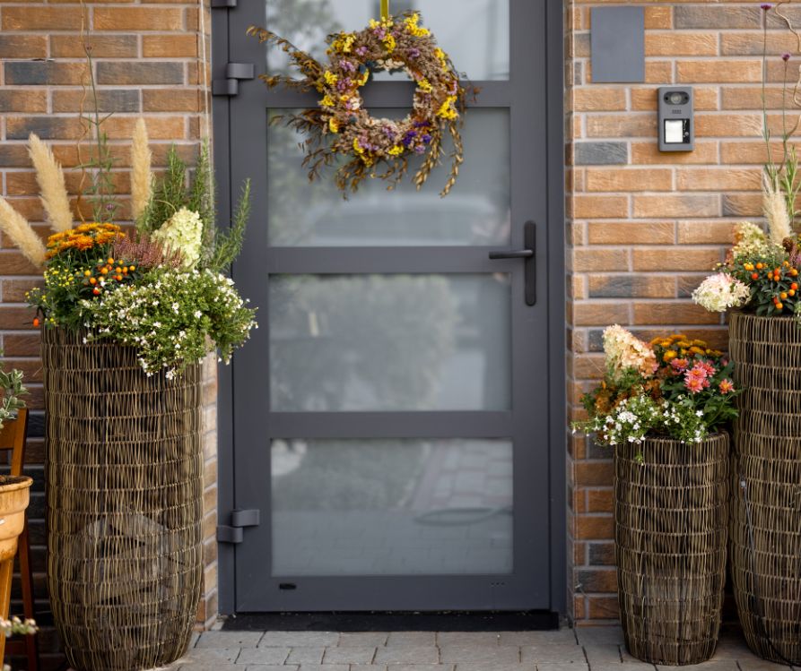 Large reed covered planter next to a front door with a fall wreath.