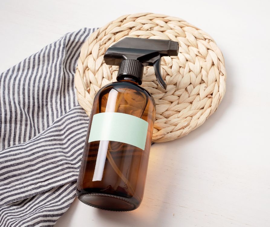 An amber spray bottle for natural cleaning products on a woven natural mat and towel.