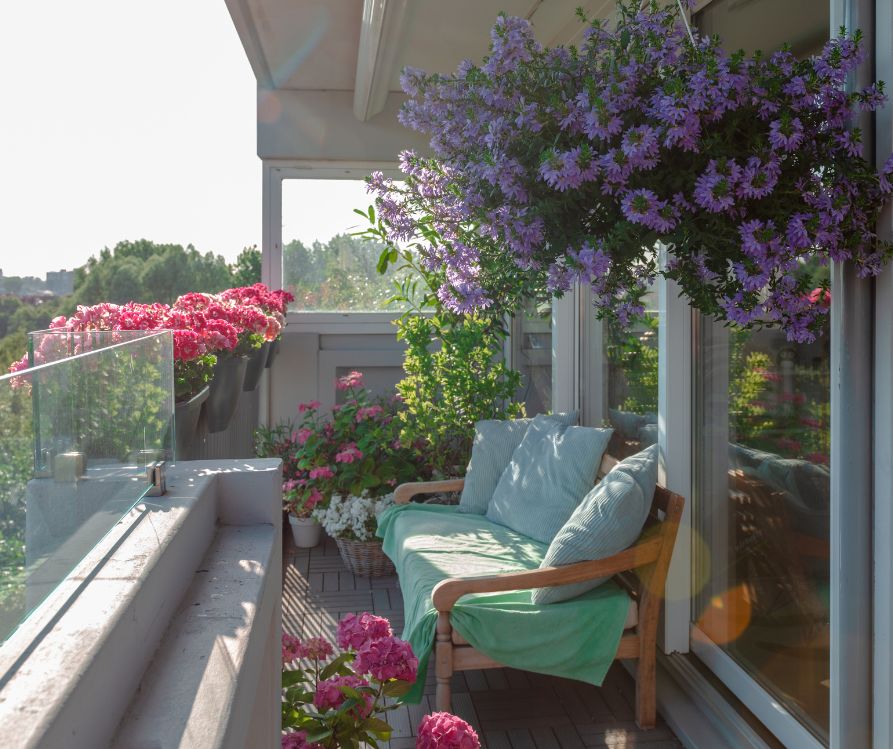 Lush flowering hanging baskets, container garden, and a compact seating area on a balcony.