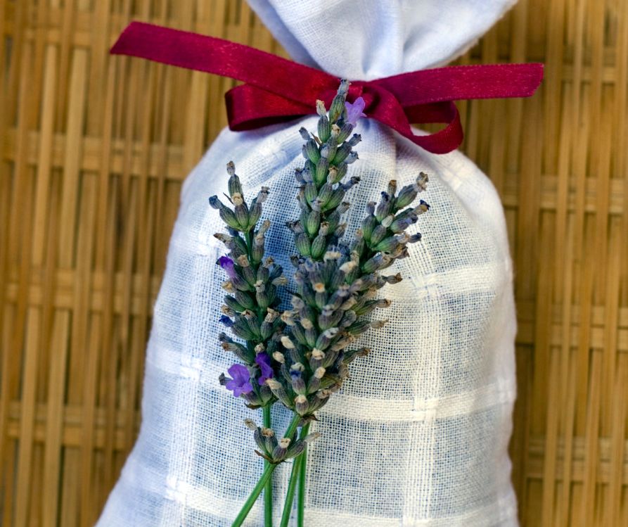 A white potpourri sachet with a red bow and sprig of lavender.