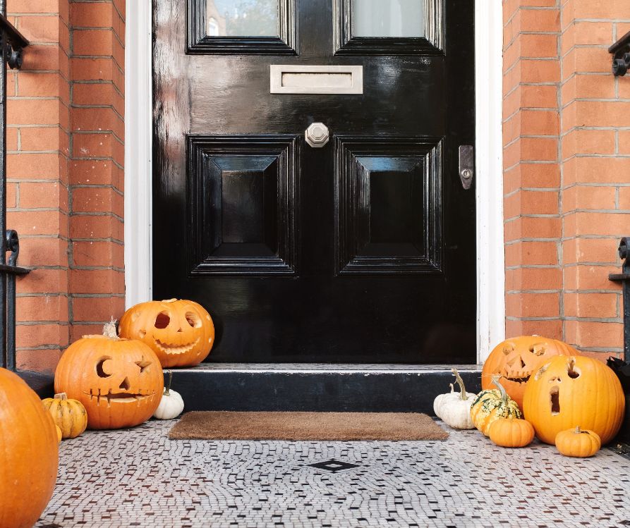 A black front door and porch surrounded by jack-o-lanterns carved to look like they are singing.