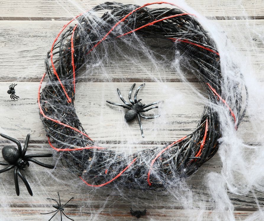 A black and orange wreath covered in faux spider webbing and plastic black spiders.