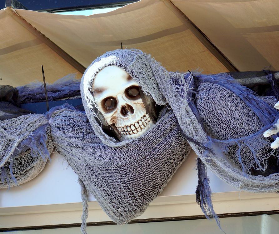 A grey cloth draped skeleton emerging from a porch cover.