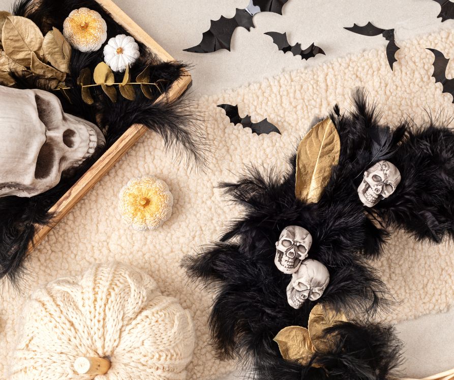 A wreath of black feathers, white and gold skulls next to a white knit pumpkin.