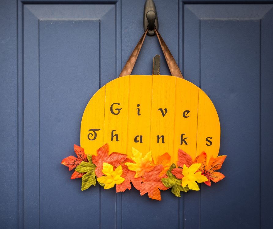 A homemade autumn door sign of a pumpkin and fall leaves. It reads, Give Thanks.