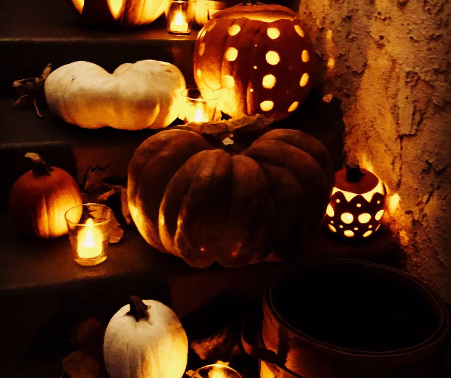 Entry way stairs decorated with pumpkins, candles, and creatively carved and illuminated squash at night.