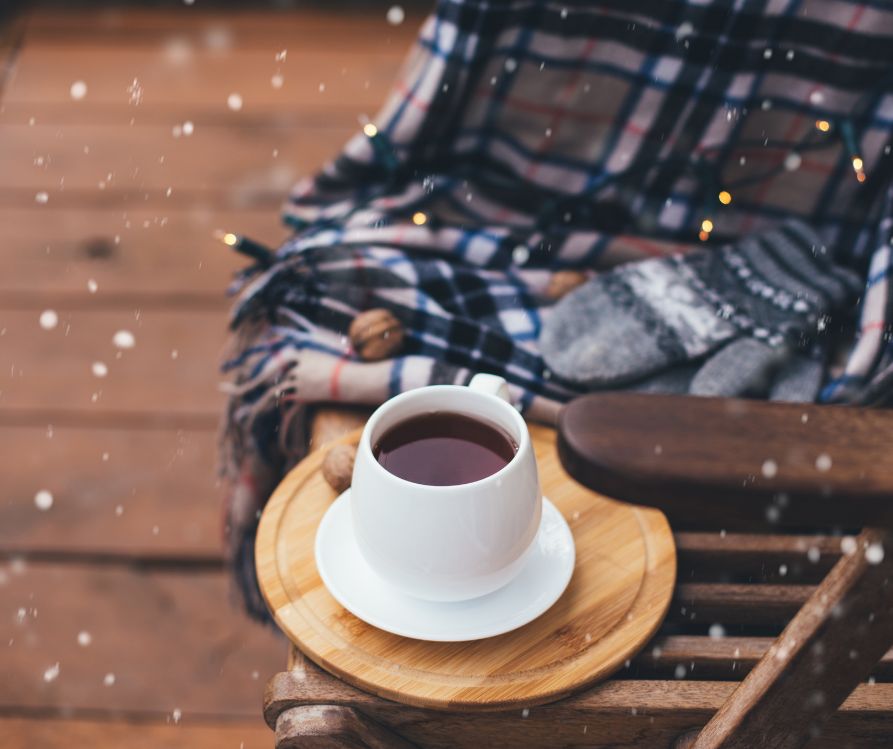 A cozy patio featuring a cup of coffee on a table next to a wooden chair and blanket.