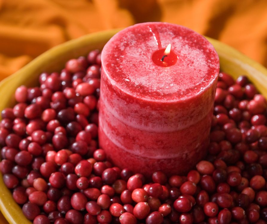 A festive red candle nestled in a deep bed of red cranberries.