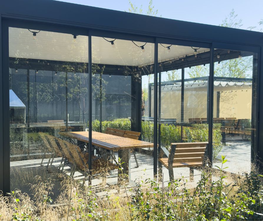 A large pergola cover a patio dinning set enclosed by clear panels to keep heat in.