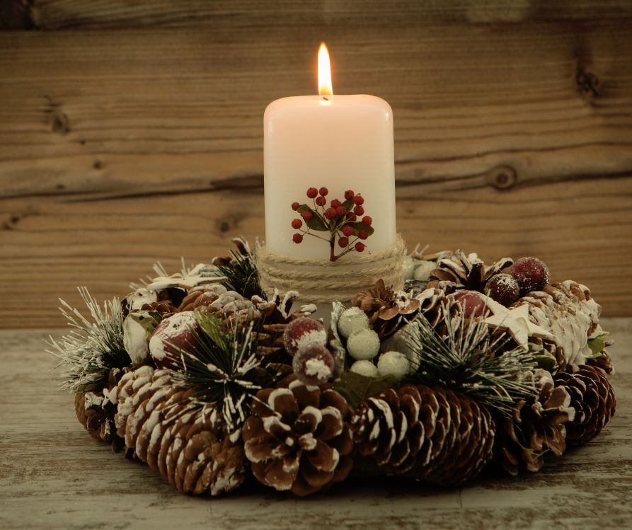 A winter centerpiece using natural elements including pinecones and evergreen frond. A white pillar candle is in the center.