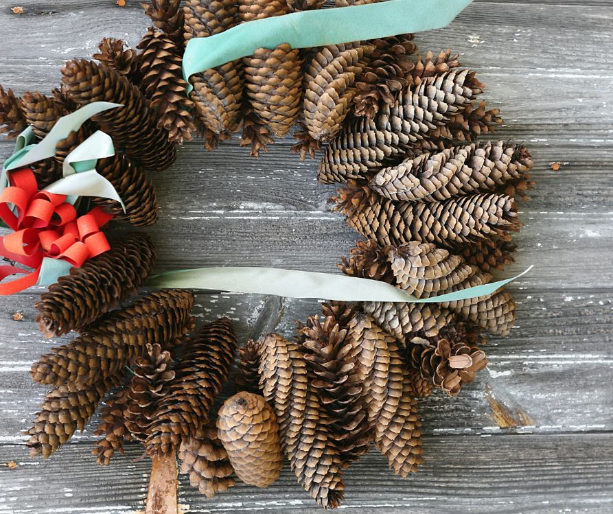 A homemade winter pinecone wreath with blue and white ribbon tied on it.