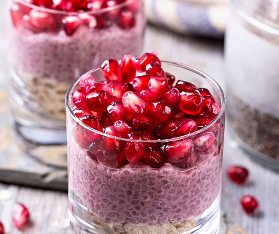 Small clear glasses of pink chia pudding topped with pomegranate seeds.