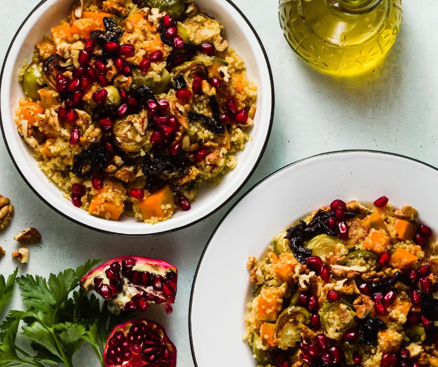 Two servings of quinoa topped with sweet potato cubes and pomegranate seeds.
