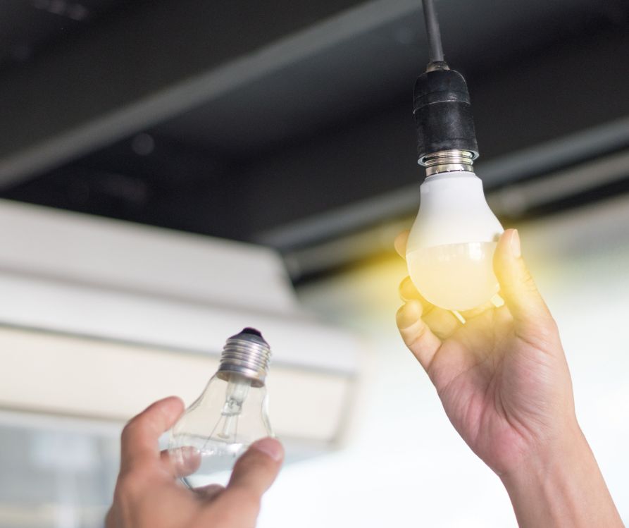 A person's hand holding a LED lightbulb and an incandescent light bulb.