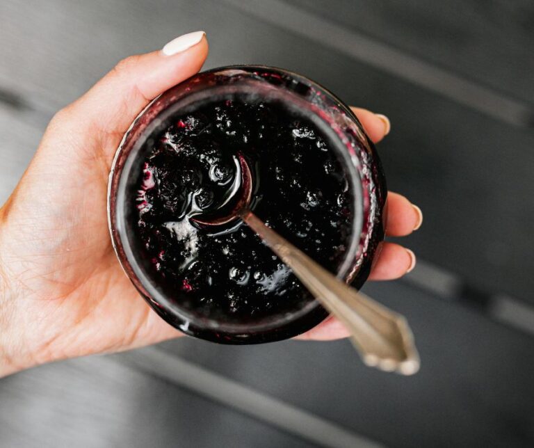 A hand holding a jar of dark purple jelly.