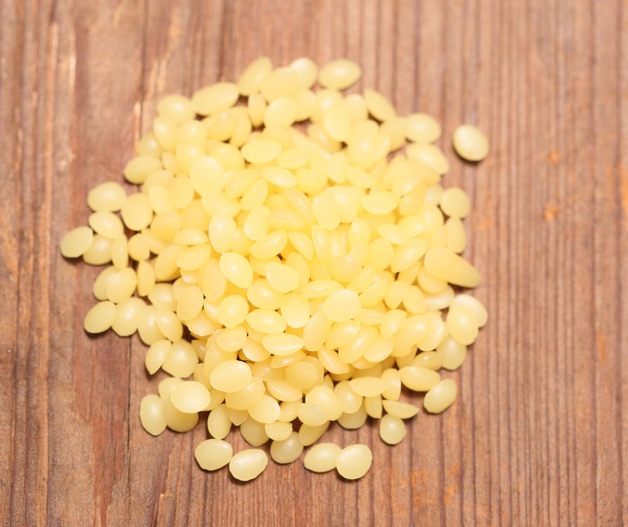 A pile of small yellow beeswax pellets on a wooden table.
