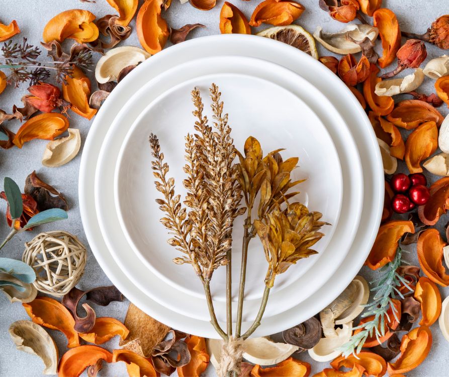 White dinner plates surround by bright dried petals and topped with dried foliage.