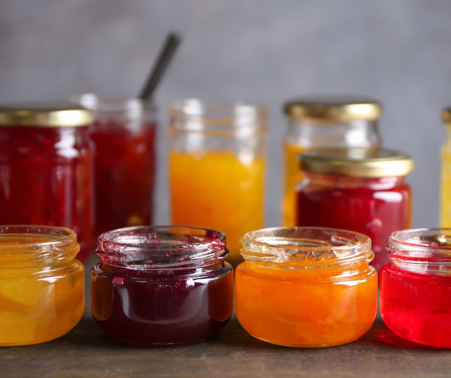 An assortment of brightly colored home made jellies in jars on a table.