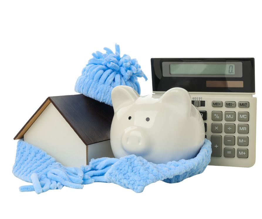 A white piggy bank and small toy home wrapped in a light blue scarf next to a calculator.