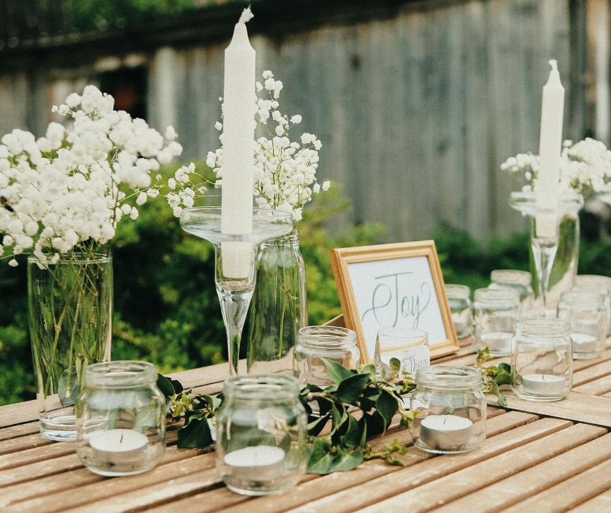 A table decorated with fresh white flowers, white candles, a sign with with word "joy" on it.