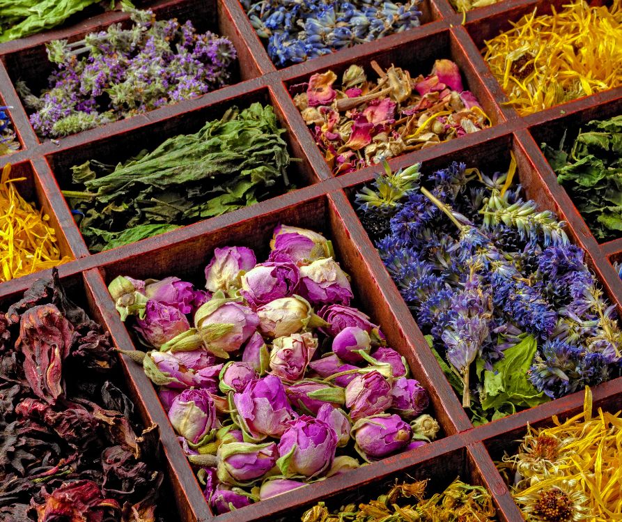 A wooden box filled with sections of dried herbs and colorful flowers.