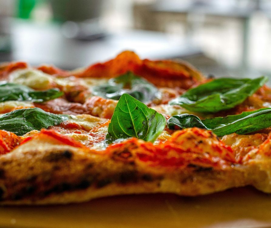 A cooked wood fire pizza topped with pepperoni and fresh basil.