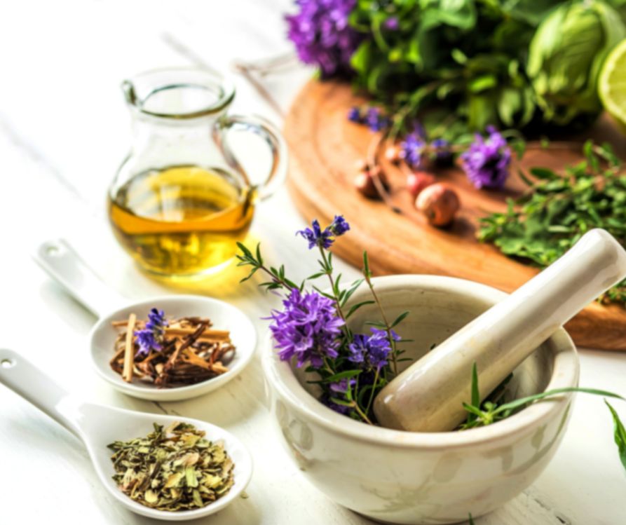 A selection of fresh and dried herbs next to a white mortal and pestle.
