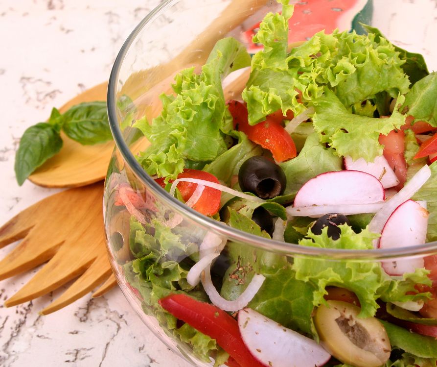 A large garden salad in a glass bowl next to wooden serving utensils.