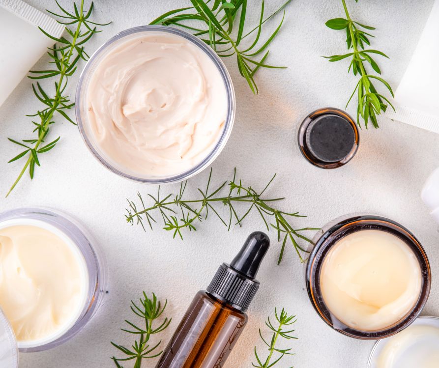Organic natural homemade cosmetics collection on a white counter next to sprigs of herbs.