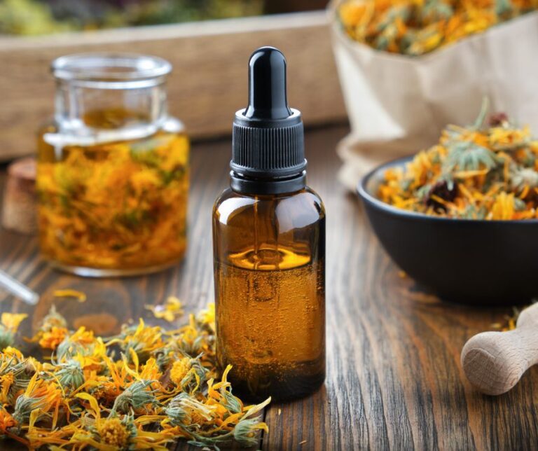 Dropper Bottle of Calendula Oil on a wooden table surrounded by dried calendula flowers.