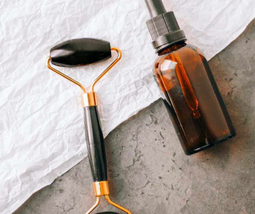 Face Roller and herbal face serum on a white towel.