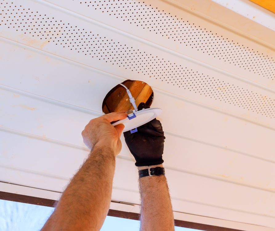 Homeowner repairs damaged soffit with lighting fixture in ceiling on suburban neighborhood.