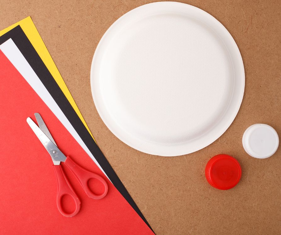 A white paper plate, red, white, black and yellow construction paper and a couple of bottle caps.