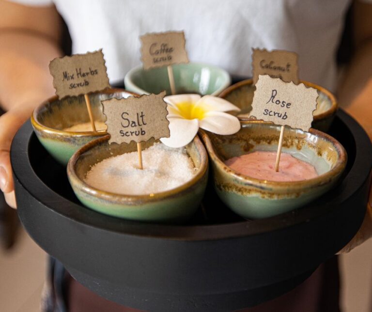 A person holding a tray of natural body scrubs with little signs in them that say rose scrub and salt scrub.
