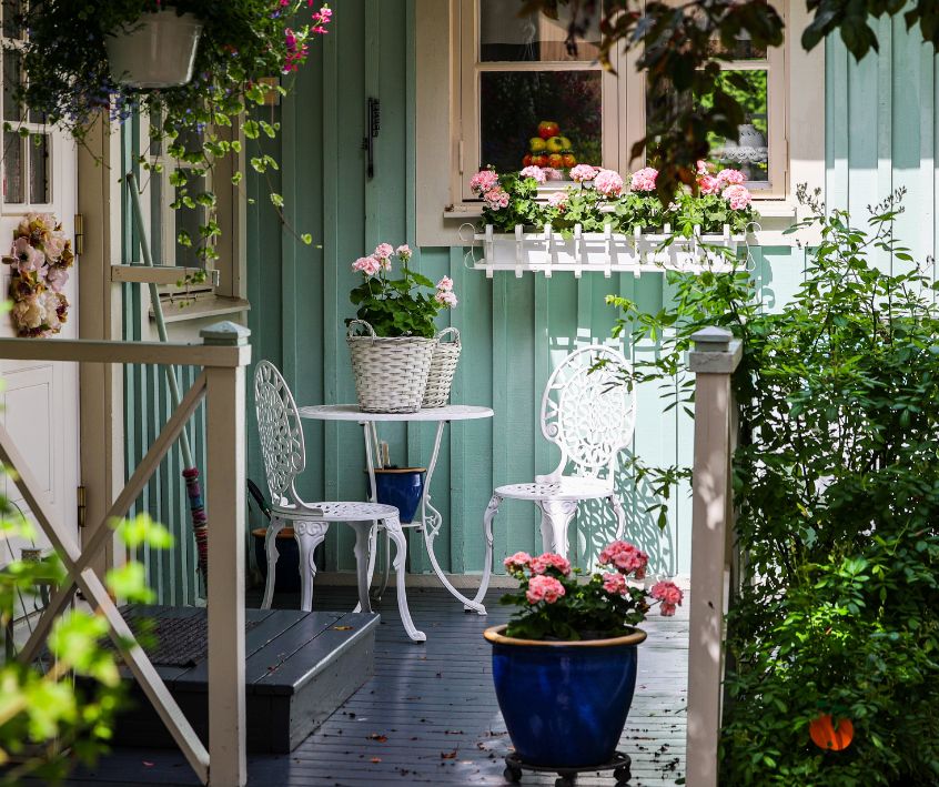 A small patio with privacy created by layers of greenery. Including hanging plants, potted plants at different heights, and green hedge.