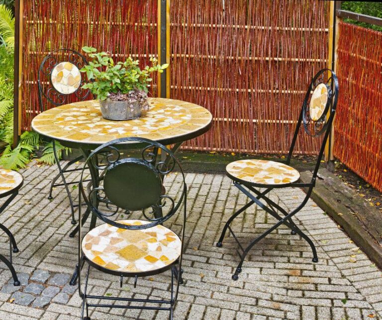 Garden chairs and table surrounded on two sides by reed privacy screens.