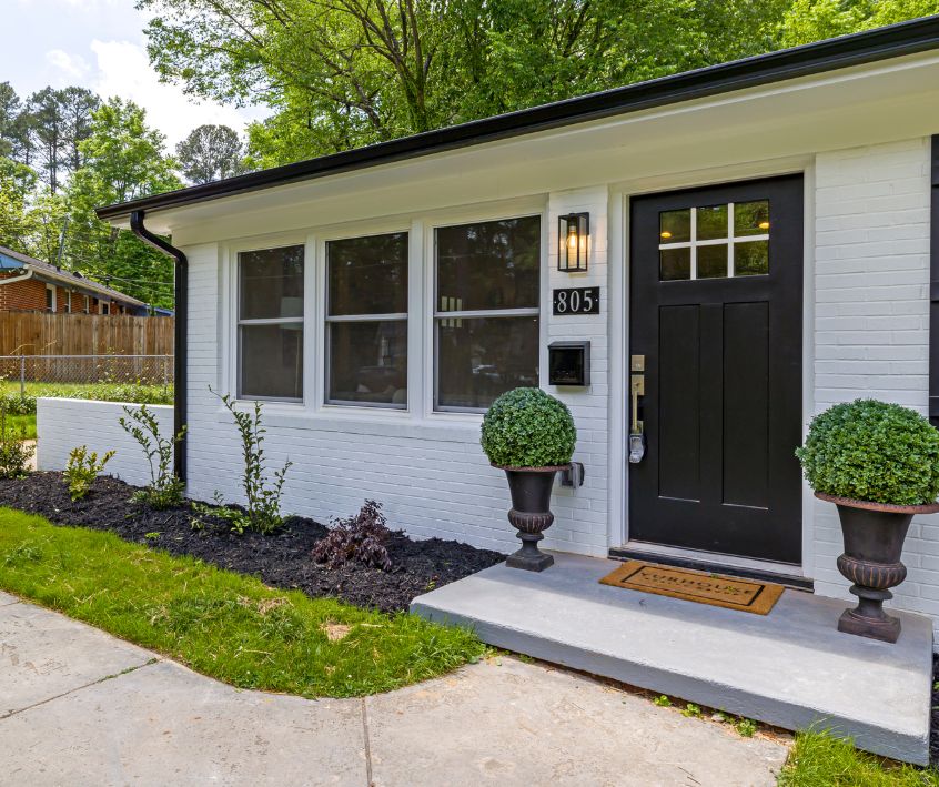 Front exterior of a family home with neat clean landscaping. Including mulched beds, edged lawn, and potted plants framing the door.