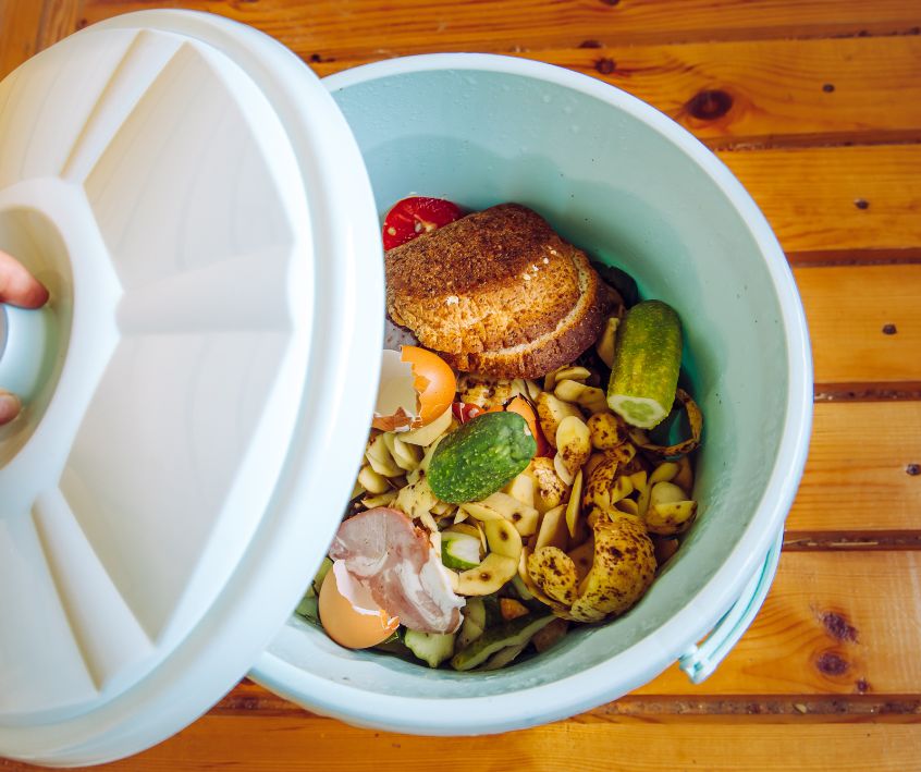 Organic food waste in white garbage bin bucket with lid in a home.