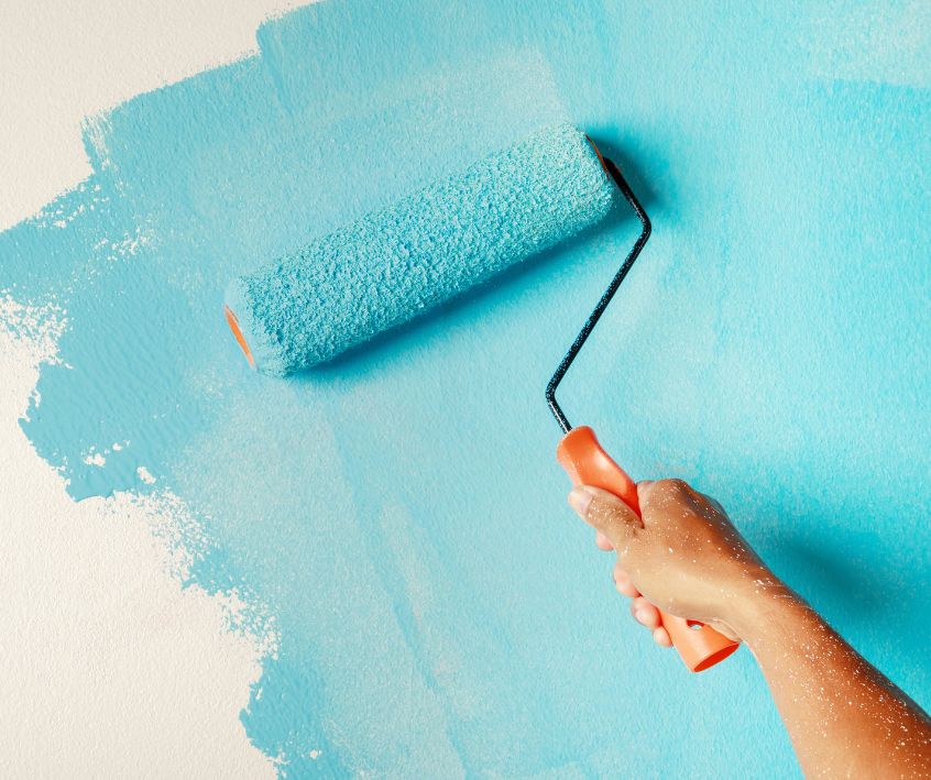 A person painting a wall blue with a roller.