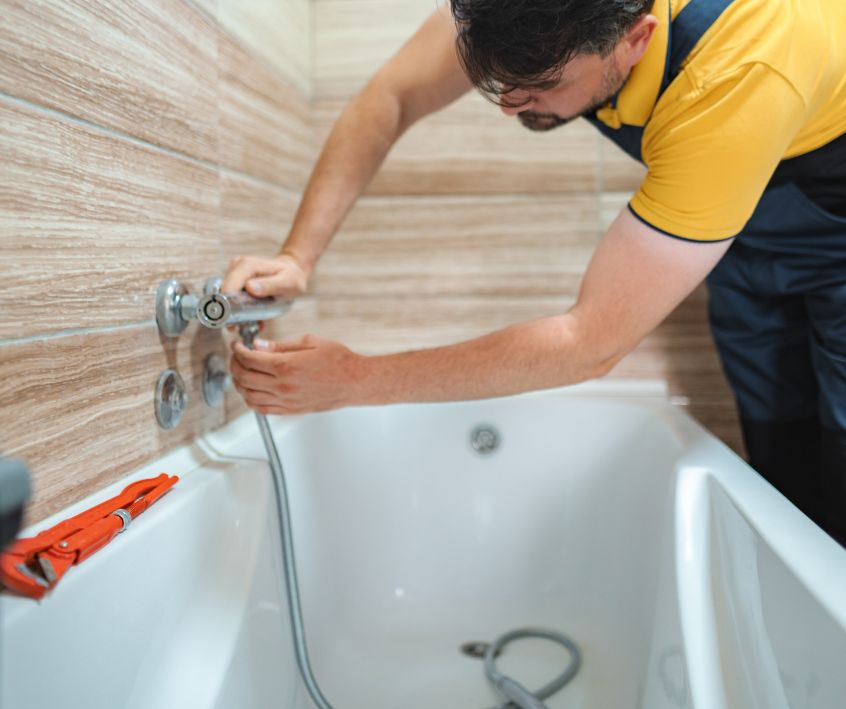 A person installing a chrome faucet on a tub in a large bathroom.