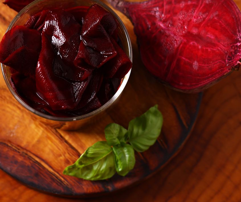 Thinly sliced pickled beets in a jar on a wooden table.