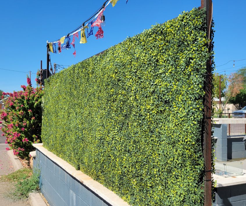A roll of green faux plants attached to fencing to provide privacy to a patio.
