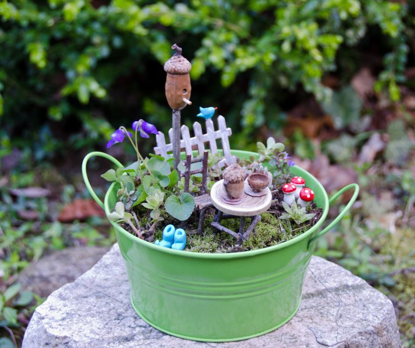 Fairy Garden Tea Time setting on a tiny round table for two in a miniature garden set in a small green metal bucket