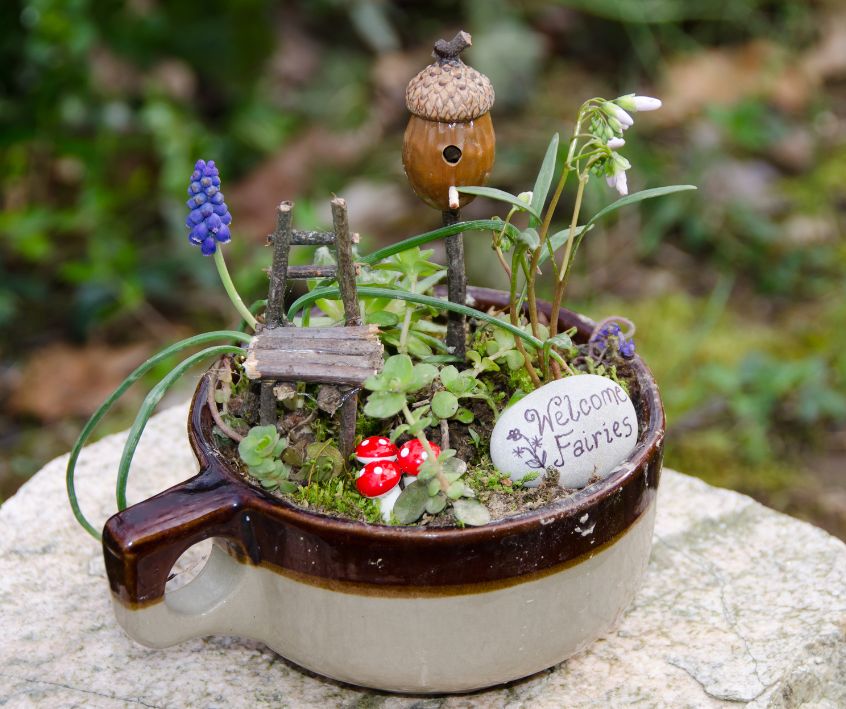 Fairy Garden in a earthen ware cup. A small house and acorn tower.