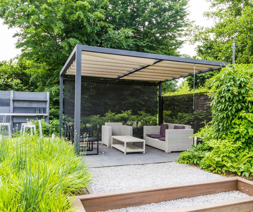 Garden sitting area under a pergola with a metal rooftop and privacy screen.
