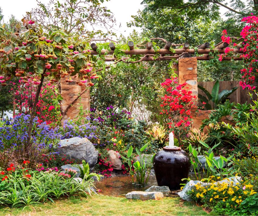 Layered flowering plants around a garden water feature.