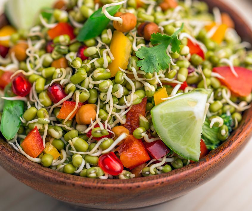 A bowl of sprouted lentil salad with herbs and tomatoes garnished with a lime wedge.